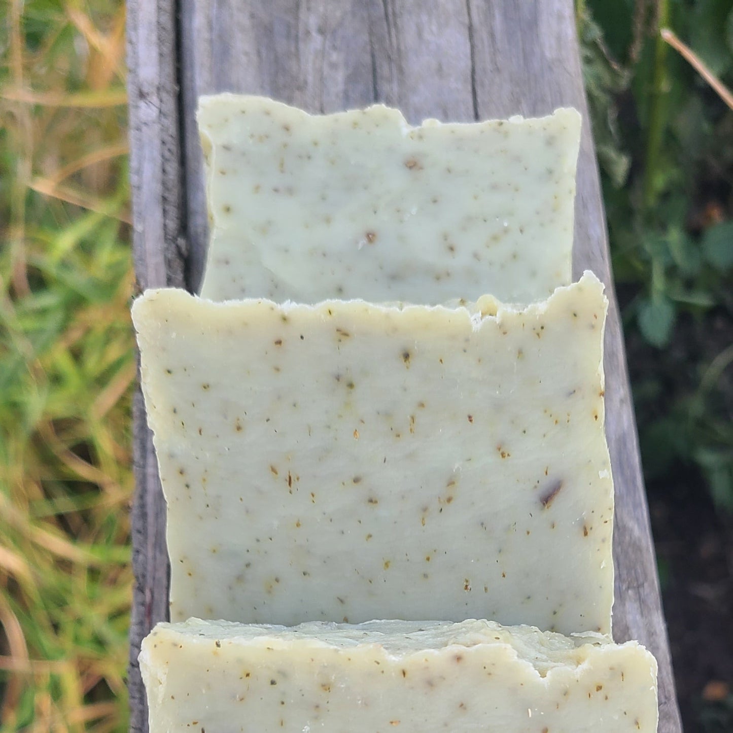 Three rectangular pieces of soap on a wooden surface with grass in the background