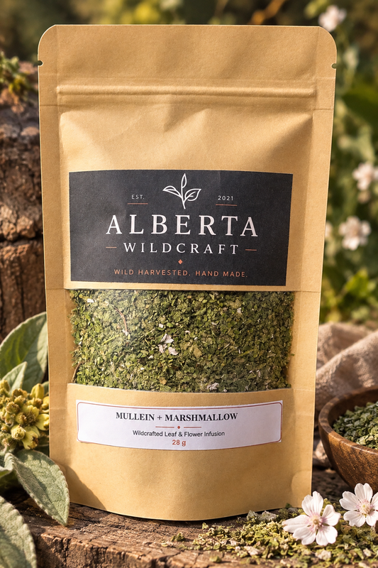 A stand-up kraft pouch of Alberta Wildcraft Mulein + Marshmallow herbal supplement, displayed on a rustic wooden surface with greenery and small white flowers in an outdoor garden setting.